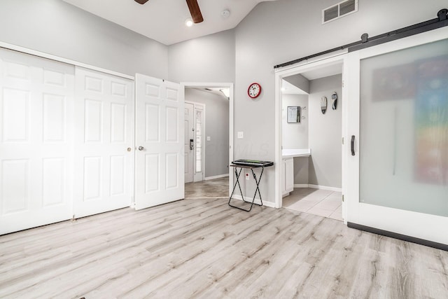 interior space with connected bathroom, vaulted ceiling, a closet, a barn door, and light hardwood / wood-style floors