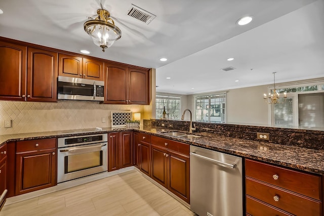 kitchen with appliances with stainless steel finishes, sink, backsplash, dark stone counters, and hanging light fixtures