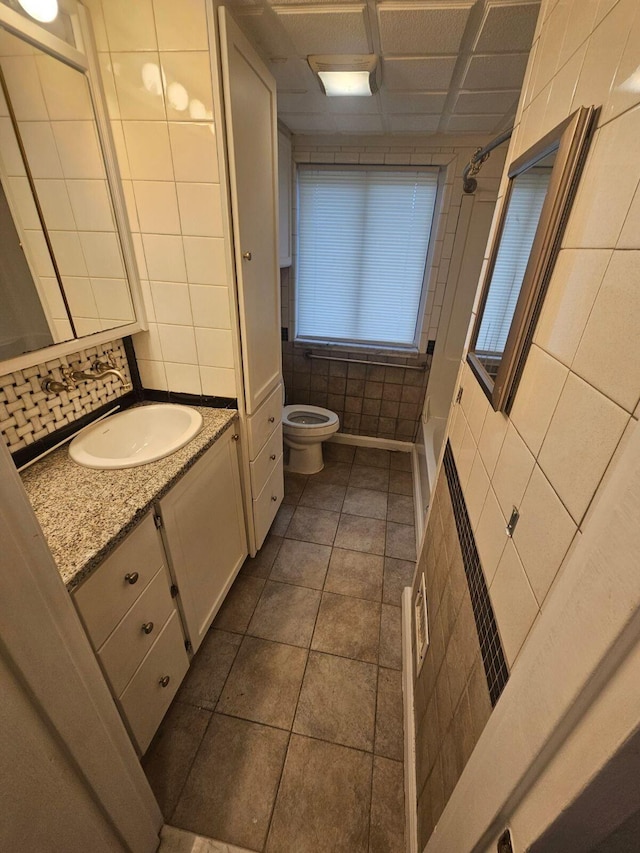 bathroom with tile patterned flooring, tile walls, vanity, tasteful backsplash, and toilet