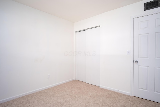 unfurnished bedroom with light colored carpet and a closet