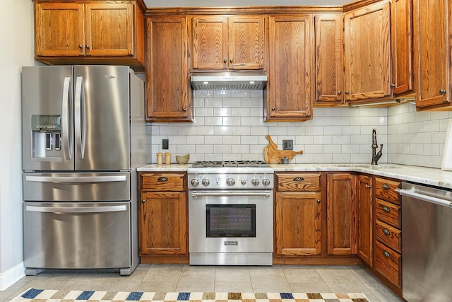 kitchen featuring sink, backsplash, stainless steel appliances, light stone counters, and light tile patterned flooring