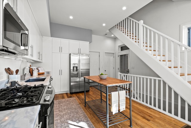 kitchen featuring appliances with stainless steel finishes, white cabinetry, wood-type flooring, sink, and a high ceiling