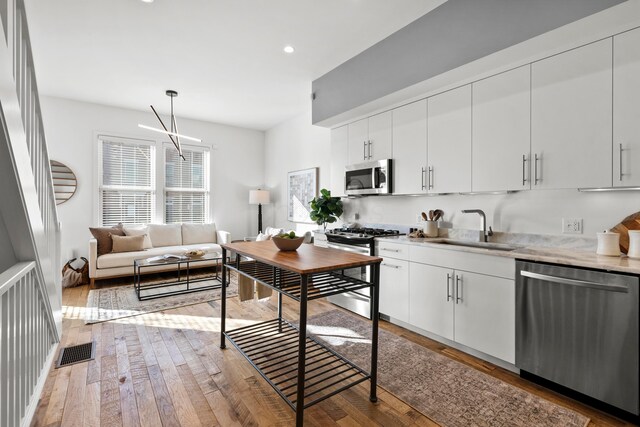 kitchen featuring sink, white cabinetry, hanging light fixtures, appliances with stainless steel finishes, and hardwood / wood-style floors