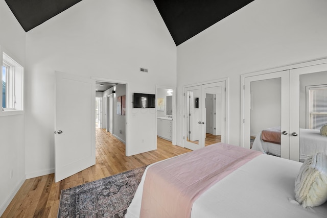 bedroom with ensuite bath, light hardwood / wood-style flooring, high vaulted ceiling, french doors, and multiple closets