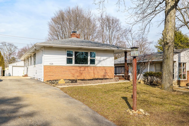 view of front facade with an outbuilding, a garage, brick siding, a front lawn, and a chimney