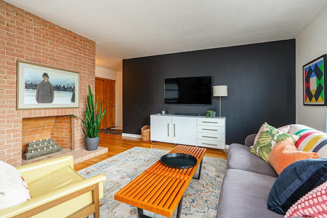 living room with a brick fireplace, an accent wall, baseboards, and wood finished floors