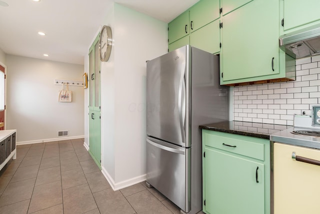 kitchen with light tile patterned floors, under cabinet range hood, visible vents, backsplash, and freestanding refrigerator