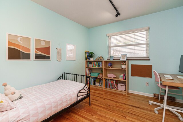 bedroom with baseboards, wood finished floors, and track lighting