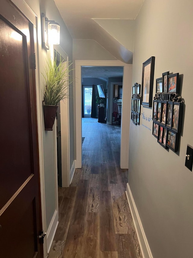 hall featuring dark wood-style floors, lofted ceiling, and baseboards