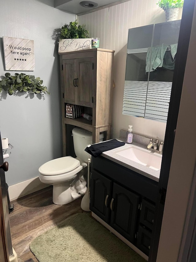 bathroom with toilet, wood finished floors, vanity, and baseboards