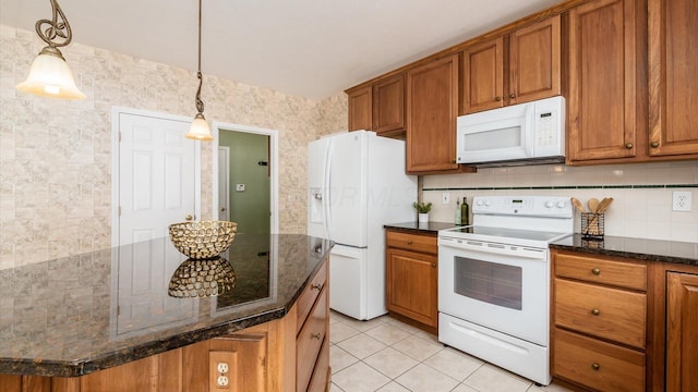 kitchen featuring light tile patterned flooring, white appliances, brown cabinets, dark stone countertops, and decorative light fixtures