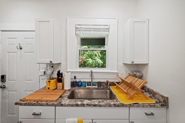 kitchen with backsplash, dark stone countertops, sink, and white cabinets