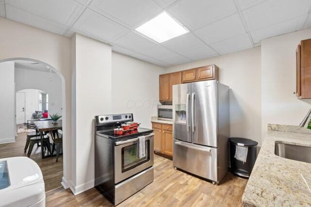 kitchen with appliances with stainless steel finishes, sink, a paneled ceiling, and light hardwood / wood-style floors