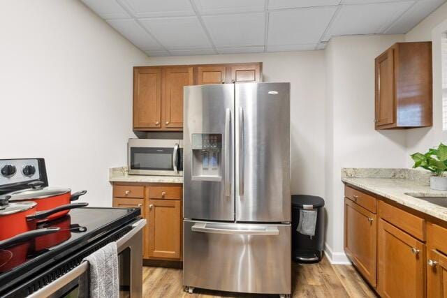 kitchen featuring a drop ceiling, light wood-type flooring, light stone countertops, and appliances with stainless steel finishes