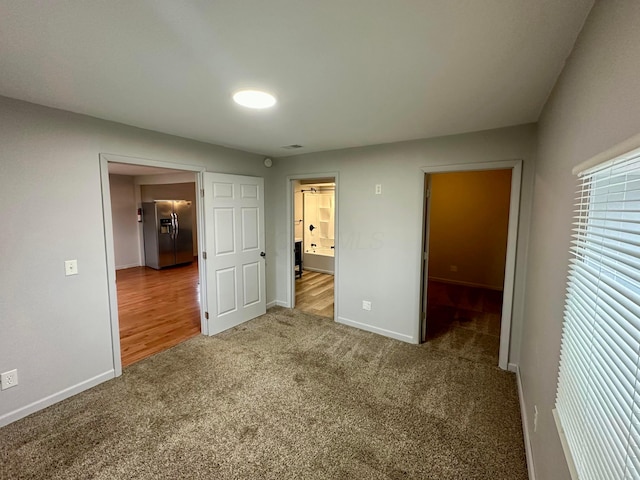 unfurnished bedroom featuring ensuite bath, stainless steel fridge, and carpet