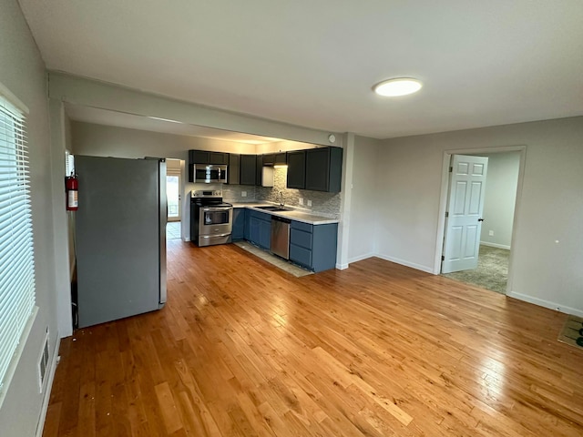 kitchen with tasteful backsplash, appliances with stainless steel finishes, sink, and light hardwood / wood-style floors