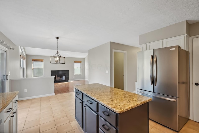 kitchen featuring white cabinets, open floor plan, a center island, freestanding refrigerator, and a fireplace