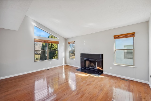 unfurnished living room with lofted ceiling, wood-type flooring, visible vents, a fireplace with flush hearth, and baseboards