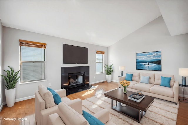 living room featuring lofted ceiling, light wood-type flooring, a glass covered fireplace, and baseboards