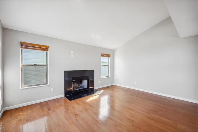 unfurnished living room featuring light wood-style floors, a fireplace with flush hearth, baseboards, and vaulted ceiling