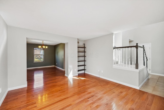 unfurnished room with a notable chandelier, visible vents, light wood-type flooring, baseboards, and stairs