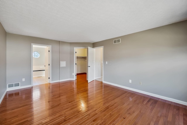 interior space with a textured ceiling, wood-type flooring, visible vents, and baseboards