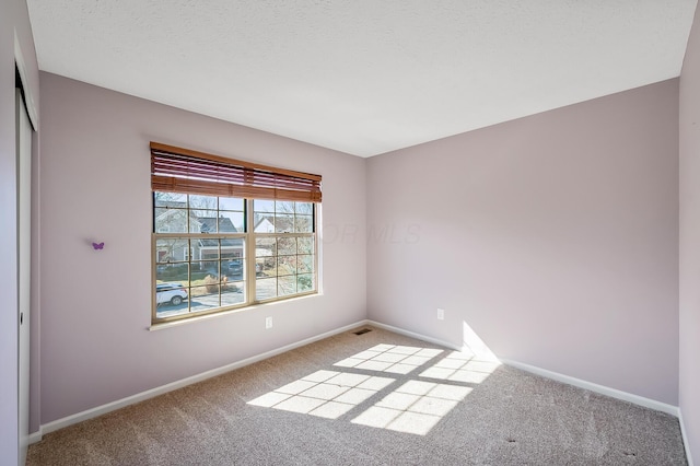 carpeted spare room with a textured ceiling and baseboards