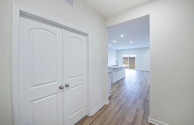 hallway featuring visible vents, baseboards, wood finished floors, a sink, and recessed lighting