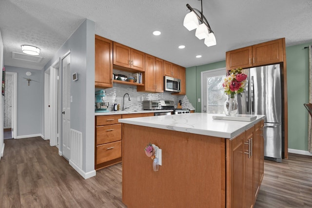 kitchen with stainless steel appliances, tasteful backsplash, wood-type flooring, a textured ceiling, and a kitchen island