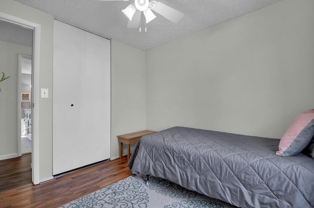 bedroom with ceiling fan, dark hardwood / wood-style floors, a textured ceiling, and a closet