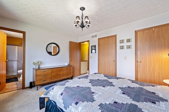 carpeted bedroom with an inviting chandelier, connected bathroom, visible vents, and a textured ceiling