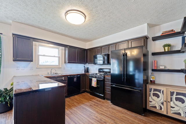 kitchen with a sink, dark brown cabinetry, light wood-type flooring, a peninsula, and black appliances