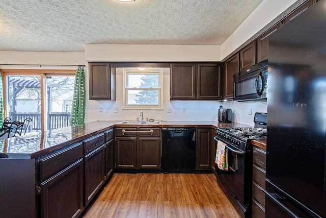 kitchen with dark brown cabinetry, light wood finished floors, a peninsula, black appliances, and a sink