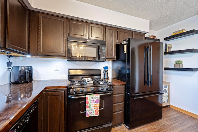 kitchen with light wood-type flooring, black appliances, a textured ceiling, and dark brown cabinets