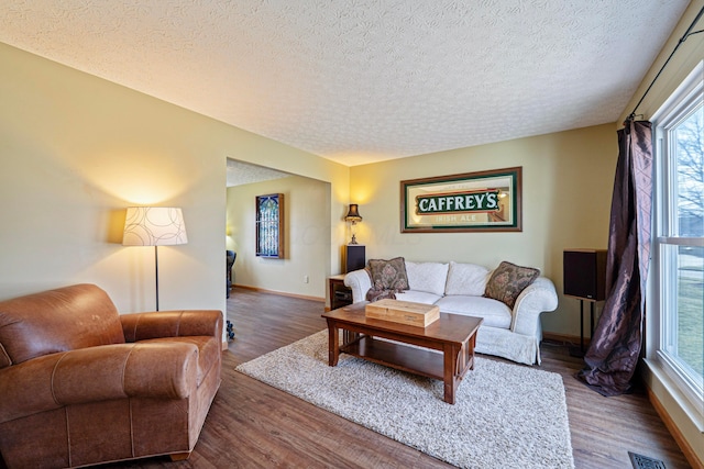 living room with visible vents, a textured ceiling, baseboards, and wood finished floors