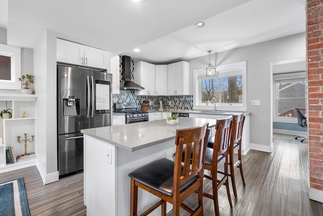 kitchen with a kitchen bar, decorative light fixtures, appliances with stainless steel finishes, a kitchen island, and wall chimney range hood