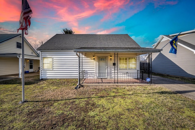 bungalow-style house with covered porch, aphalt driveway, roof with shingles, and a front yard