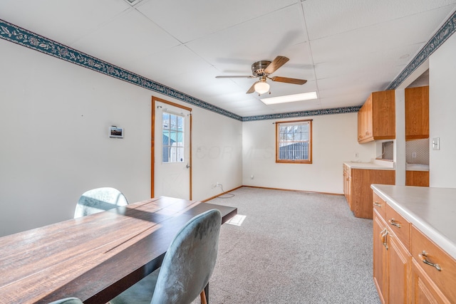 dining room with a ceiling fan, a healthy amount of sunlight, light carpet, and baseboards