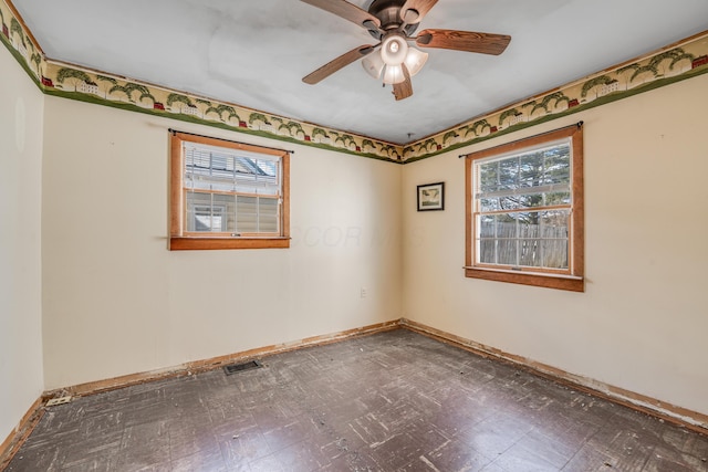 spare room with a ceiling fan, dark floors, visible vents, and baseboards