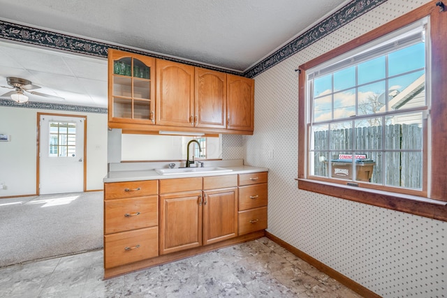 kitchen featuring a sink, baseboards, light countertops, glass insert cabinets, and wallpapered walls