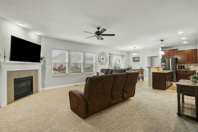 carpeted living room featuring ceiling fan, sink, a tile fireplace, and a textured ceiling