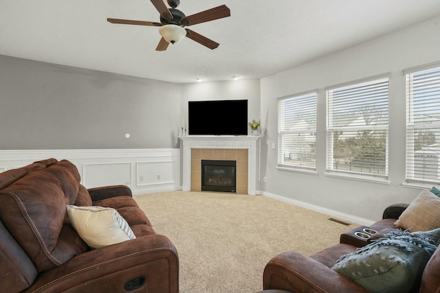 living room featuring a tile fireplace, carpet flooring, and ceiling fan