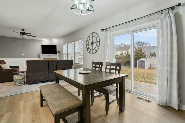 dining area with ceiling fan with notable chandelier, light hardwood / wood-style flooring, and a wealth of natural light