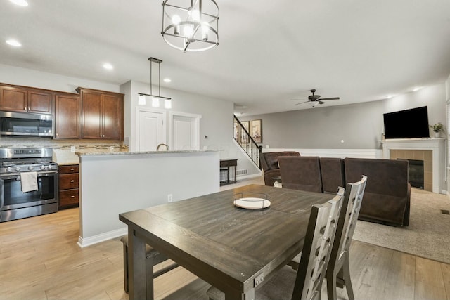 dining room with a tiled fireplace, ceiling fan, and light hardwood / wood-style flooring