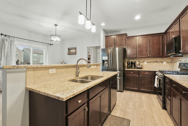 kitchen featuring pendant lighting, sink, stainless steel appliances, light stone countertops, and a center island with sink