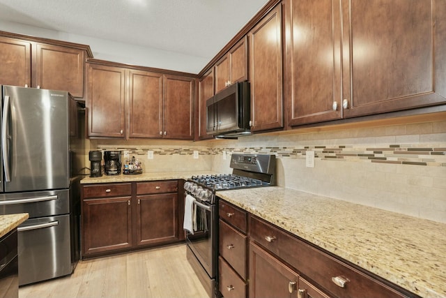 kitchen with light stone countertops, appliances with stainless steel finishes, light wood-type flooring, and decorative backsplash