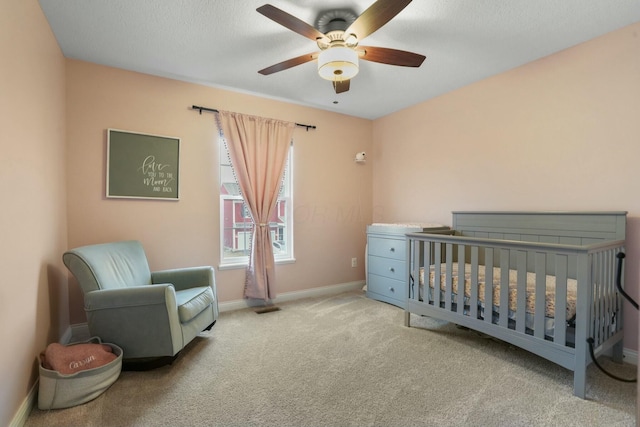 bedroom featuring a crib, light carpet, a textured ceiling, and ceiling fan