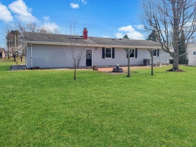 rear view of property featuring central air condition unit, a lawn, and a chimney