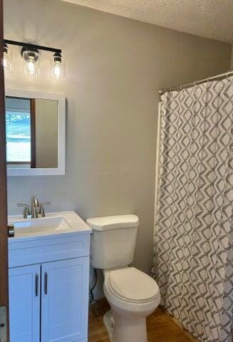 bathroom with vanity, toilet, wood finished floors, and a textured ceiling