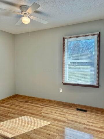 unfurnished room featuring visible vents, a textured ceiling, a ceiling fan, and wood finished floors